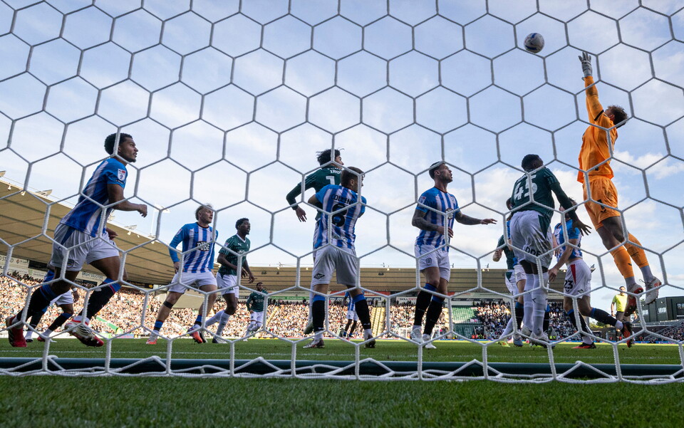Footballers compete for the ball, with one player leaping for it above the net.