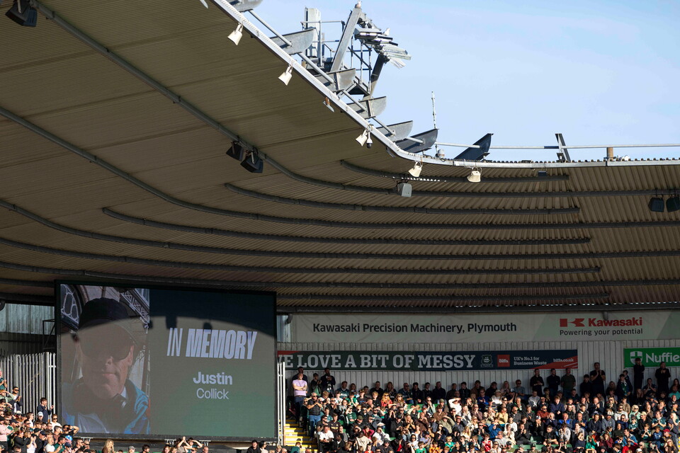 Crowd watching a memorial tribute to Justin Langer on a large screen at a sports stadium.