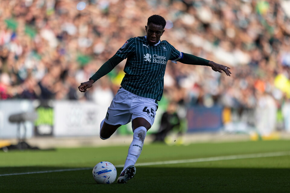 A soccer player in a green jersey and white shorts kicks a ball on a field.