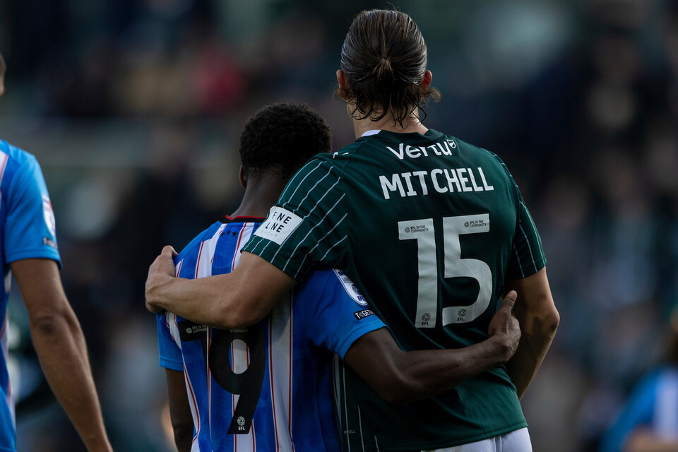 Player in green and white with "MITCHELL" and "15" on the back stands behind player in blue and white with "9" on the back