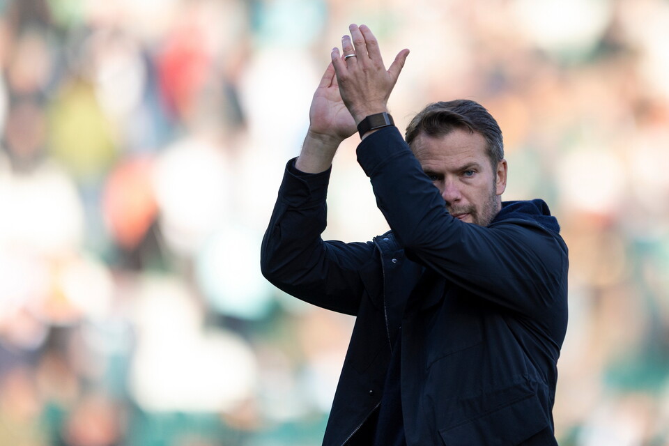 Football coach with hands raised in a stadium, acknowledging the crowd.