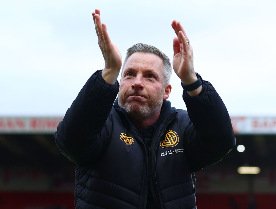 Manager with hands raised on pitch applauding crowd