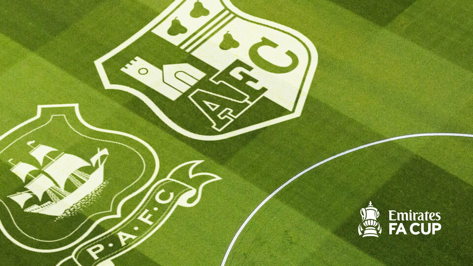 Two football club logos on a green grass background with an Emirates FA Cup logo