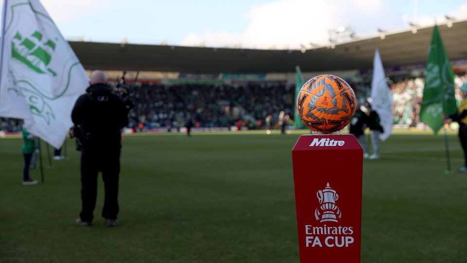 Emirates FA Cup trophy on a stand on a football pitch with a man in the background