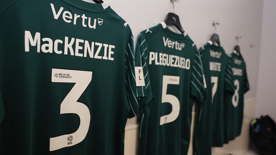 Five green football shirts with numbers 3, 5, 7, and 3 hanging on a white wall.