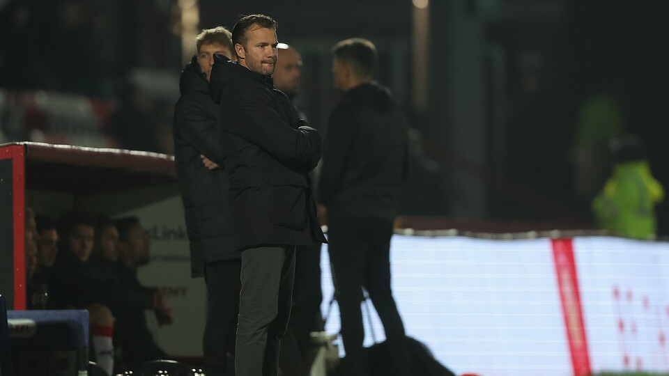 Four men stand on a football pitch; two are looking out at the pitch.
