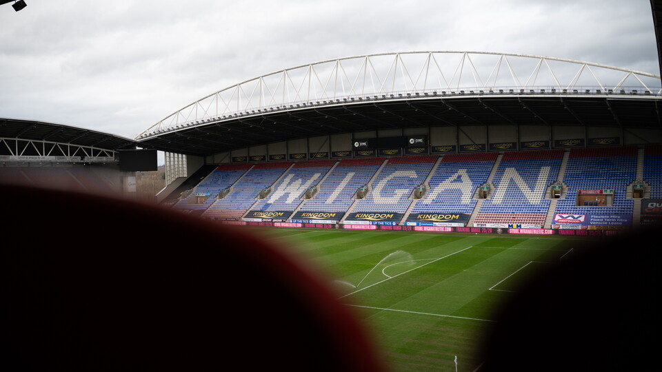 Empty stadium with Wigan written on the seats under a cloudy sky