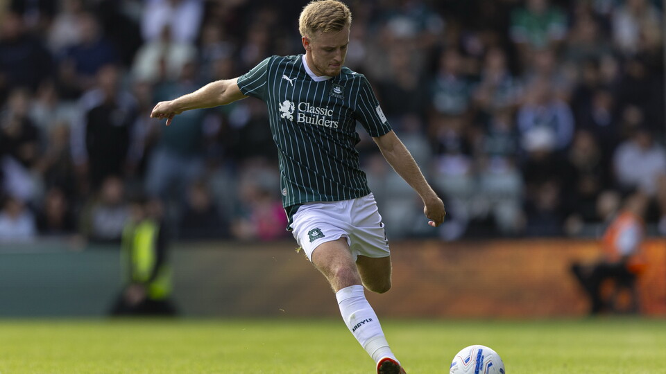 Football player in green and white kit kicking ball on green pitch.