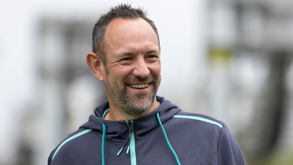 A man in a blue hoodie with green stripes smiles for a photo outside.