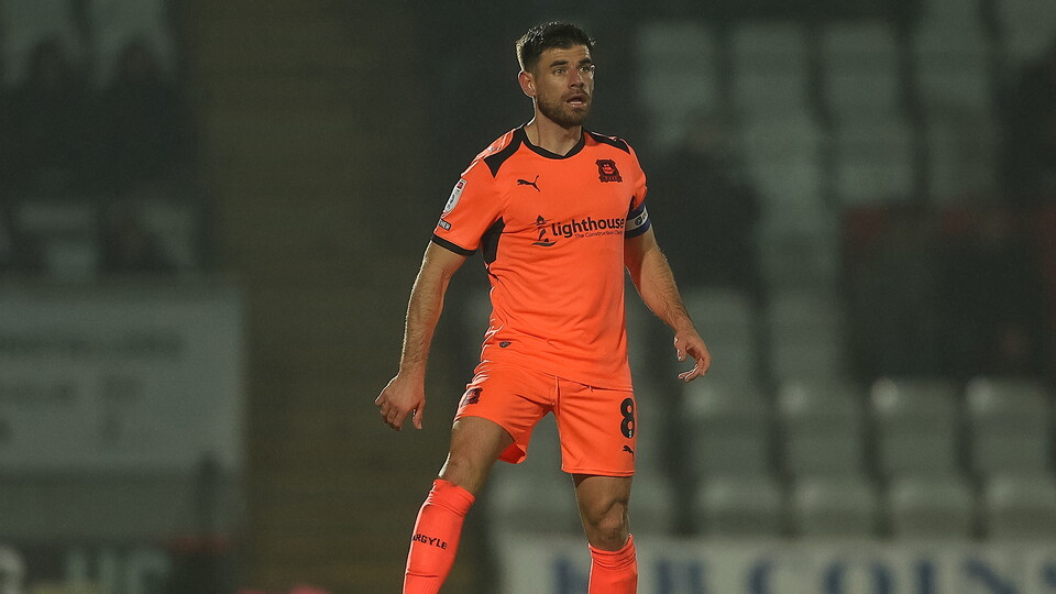 Footballer stands in an orange strip on a football pitch.