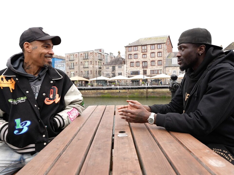 MC Harvey and Brendan Wiredu in conversation on a bench by the Barbican, Plymouth.