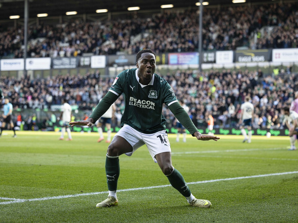 Soccer player in green celebrating a goal in front of a crowd.
